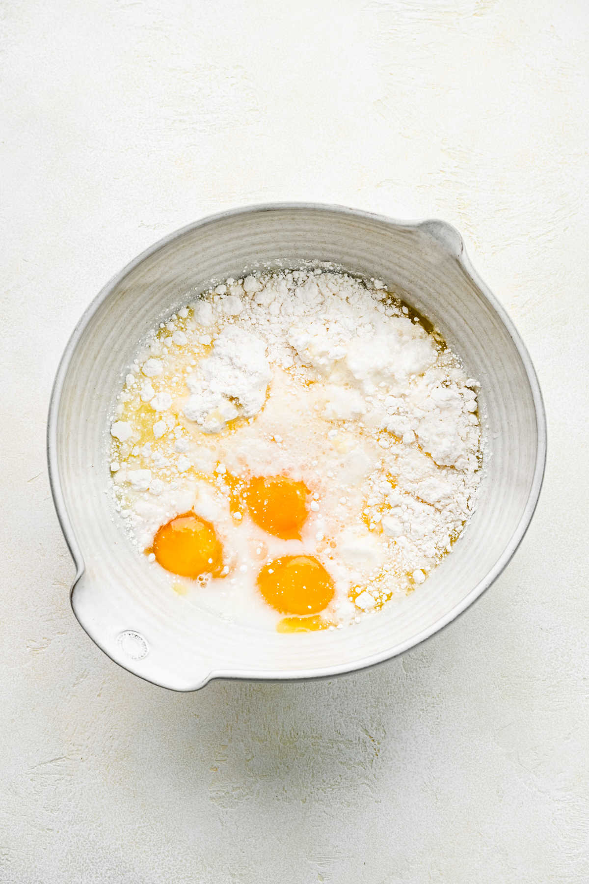Cake mix, eggs, water, and milk in a ceramic mixing bowl. 
