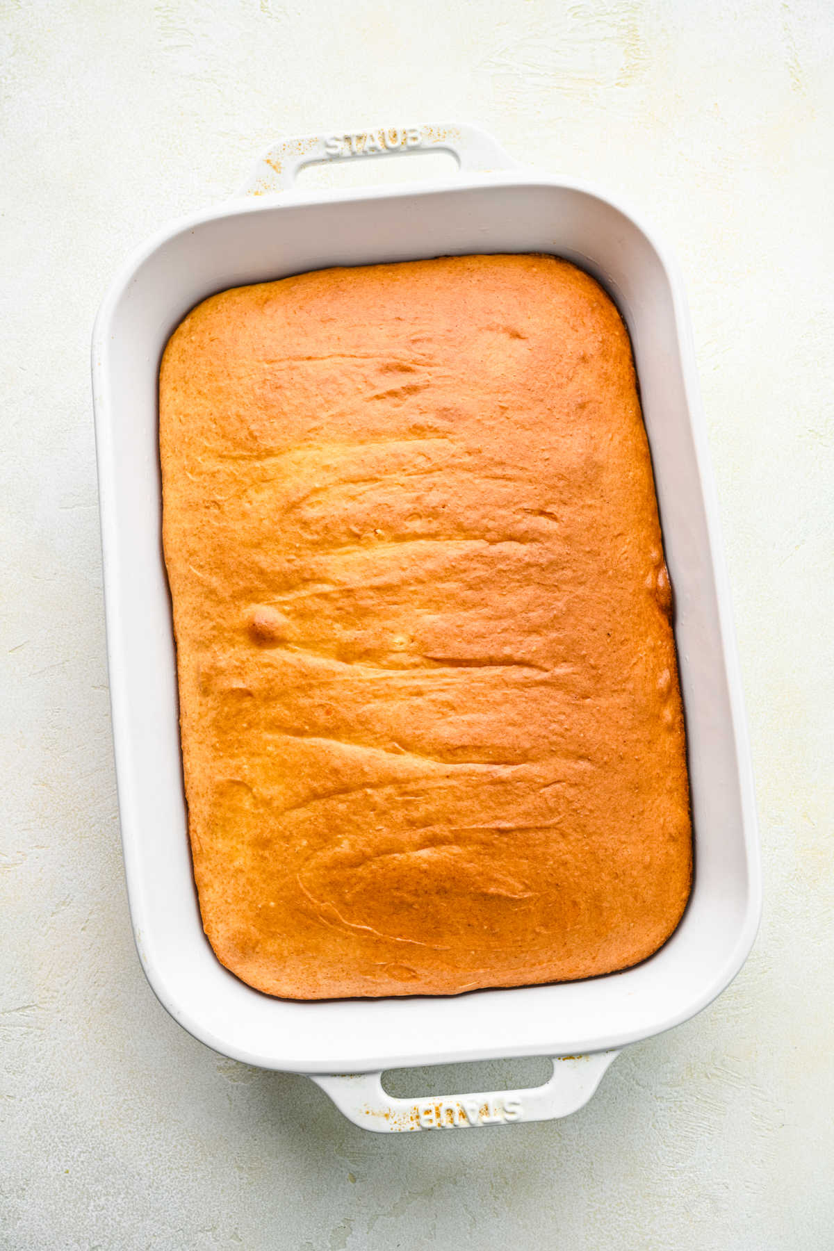 Baked cinnamon roll poke cake in a white baking pan.