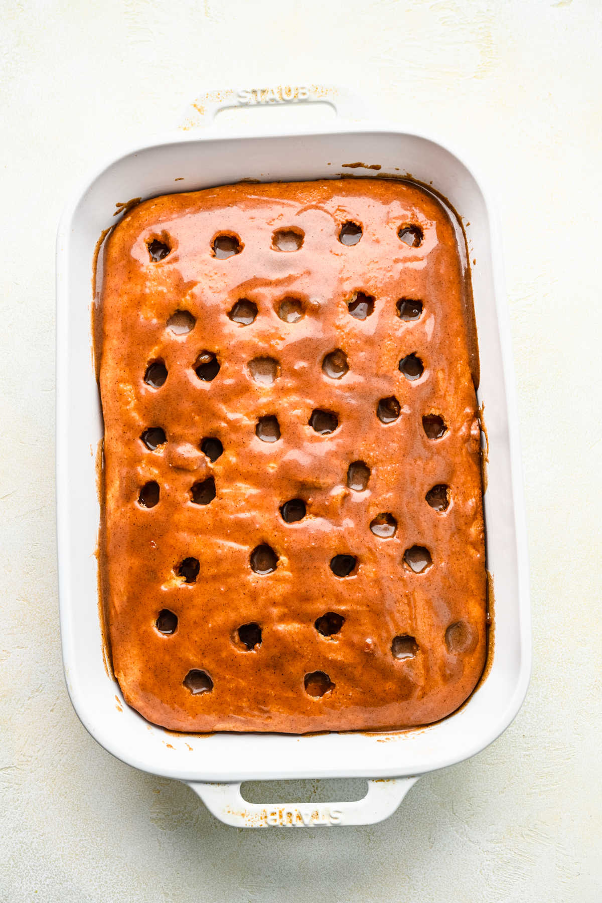 Cinnamon filling poured over baked cinnamon roll poke cake.