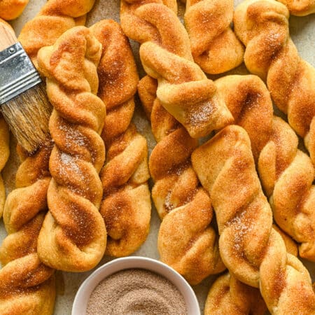 Cinnamon breadsticks piled around a white dish of cinnamon sugar.