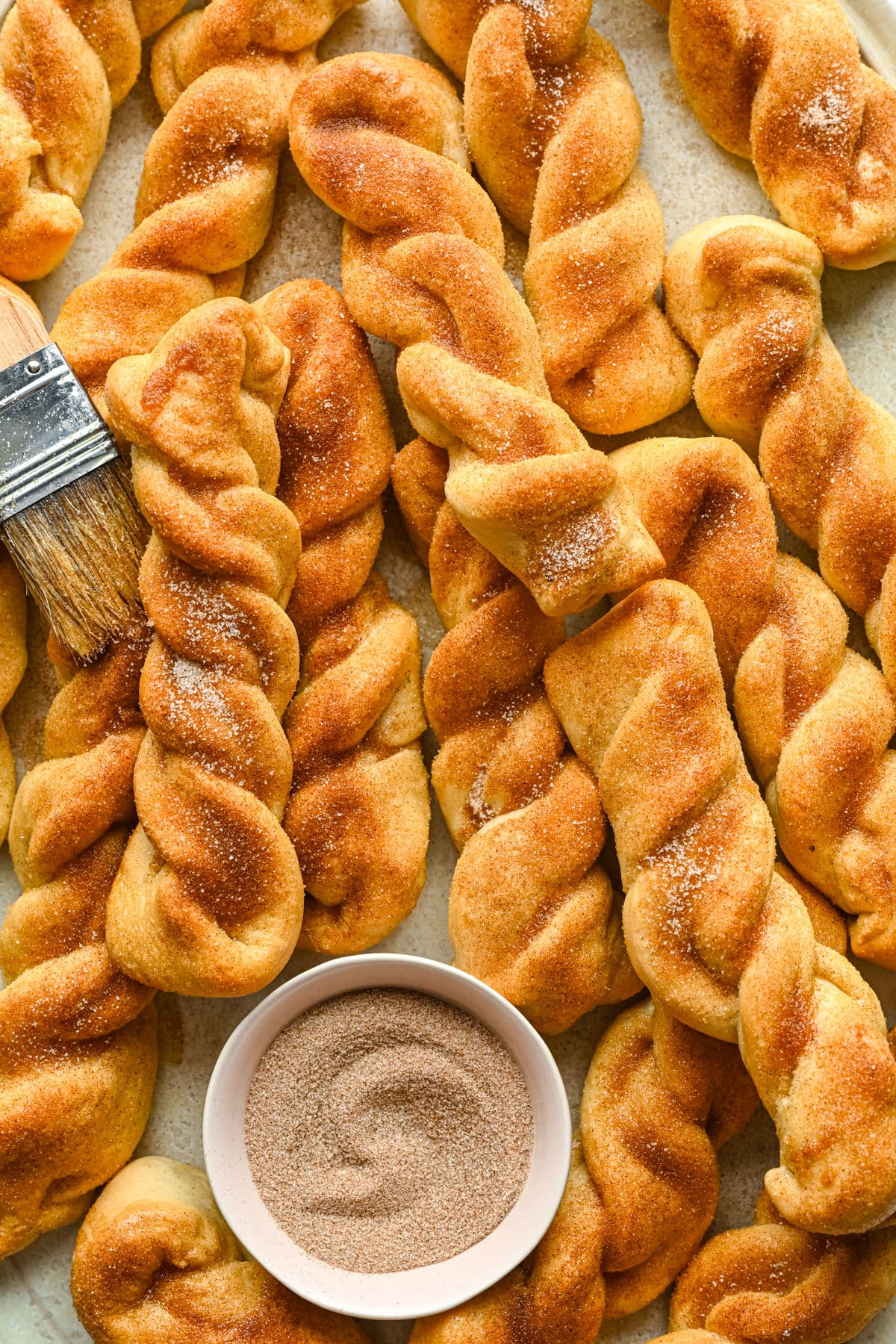 Cinnamon breadsticks piled around a white dish of cinnamon sugar. 