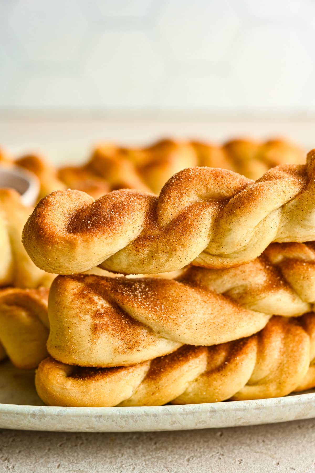 Three cinnamon breadsticks stacked on top of each other on a white plate.