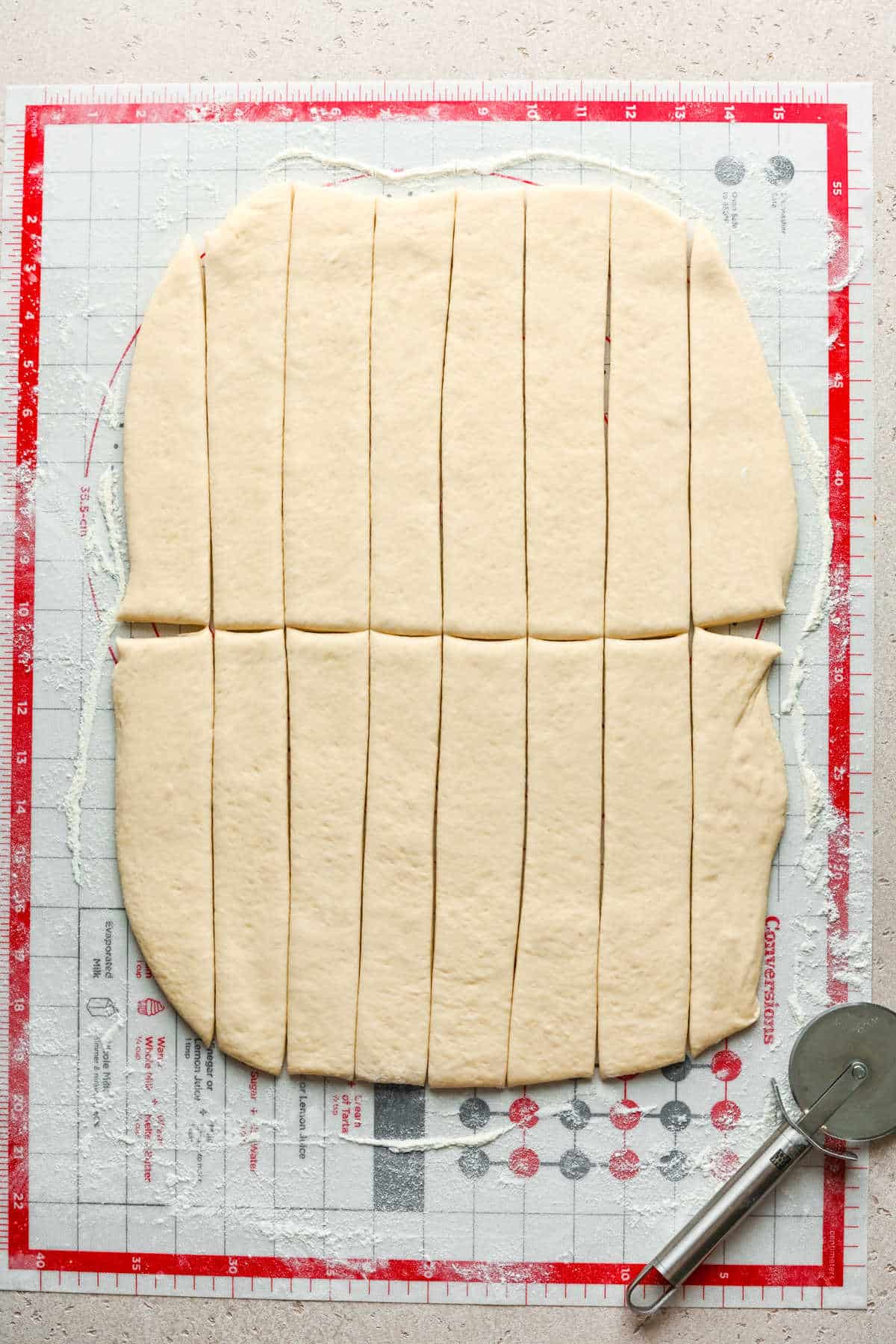 Cinnamon breadstick dough cut into strips on a baking mat.