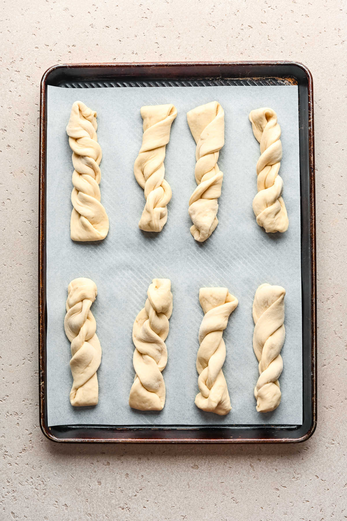 Unbaked cinnamon breadsticks on a parchment lined baking sheet. 