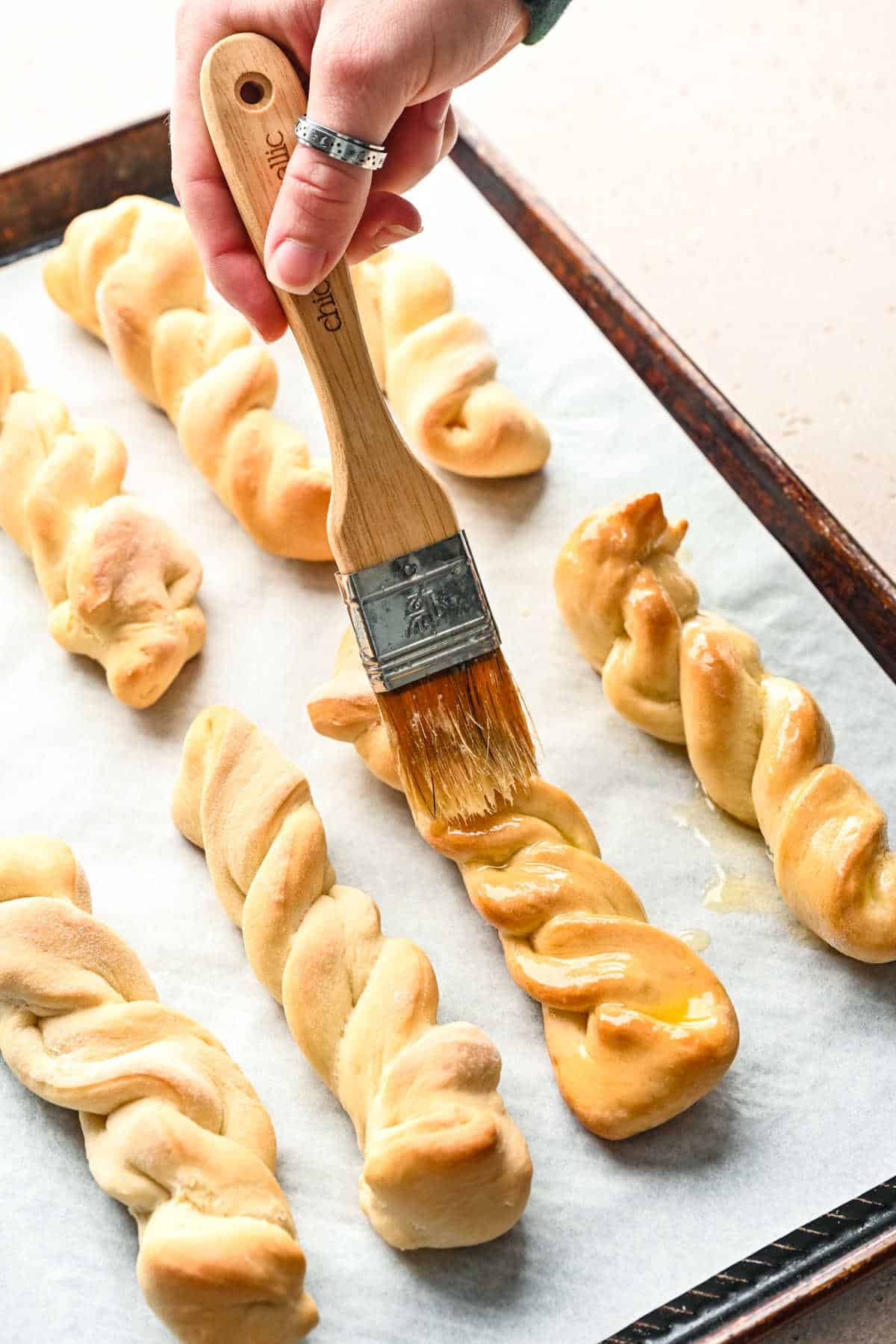 A basting brush brushing melted butter onto baked cinnamon breadsticks.