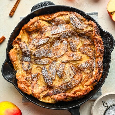 German apple pancake dusted with powdered sugar in a cast iron skillet.