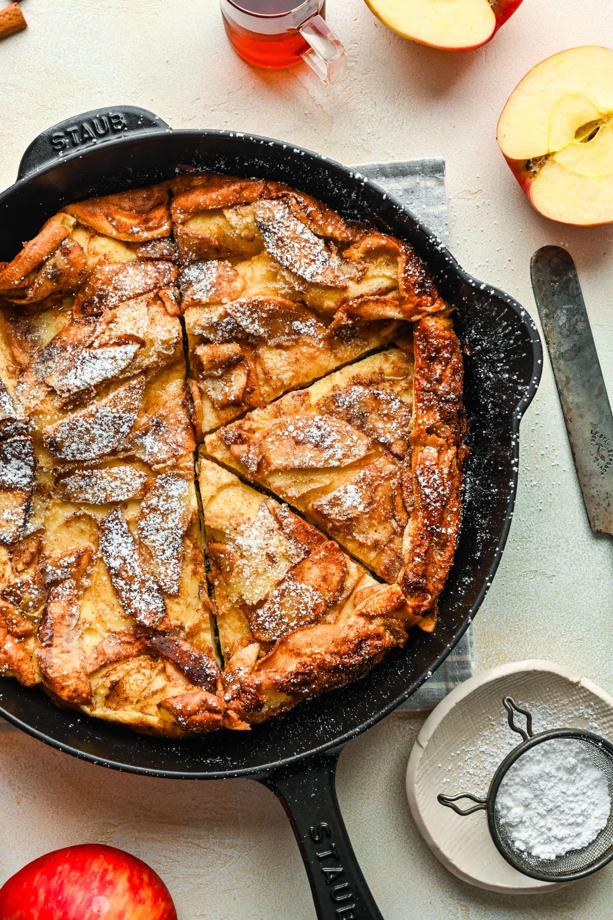 A powdered sugar dusted German apple pancake cut into pieces in a cast iron skillet.