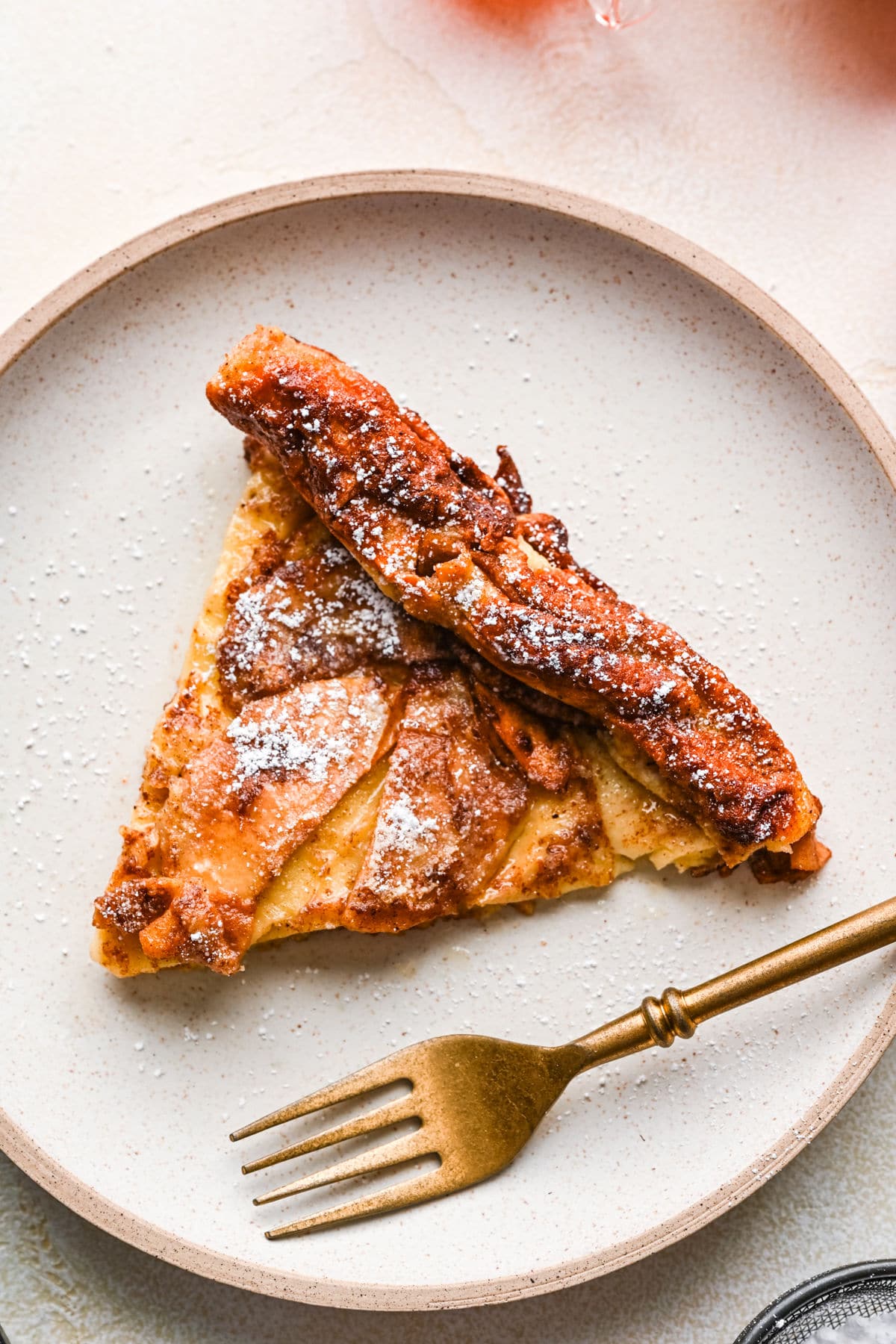 A slice of German apple pancake on a plate with a gold fork.