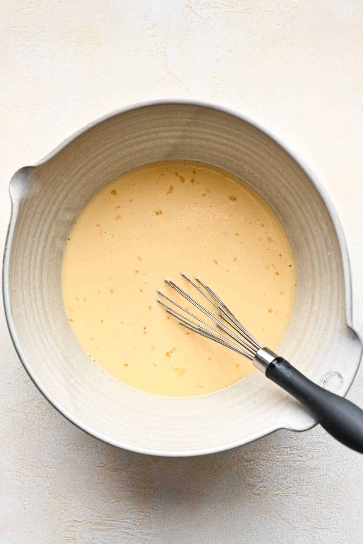 Egg and milk mixture for German apple pancake in a ceramic mixing bowl. 