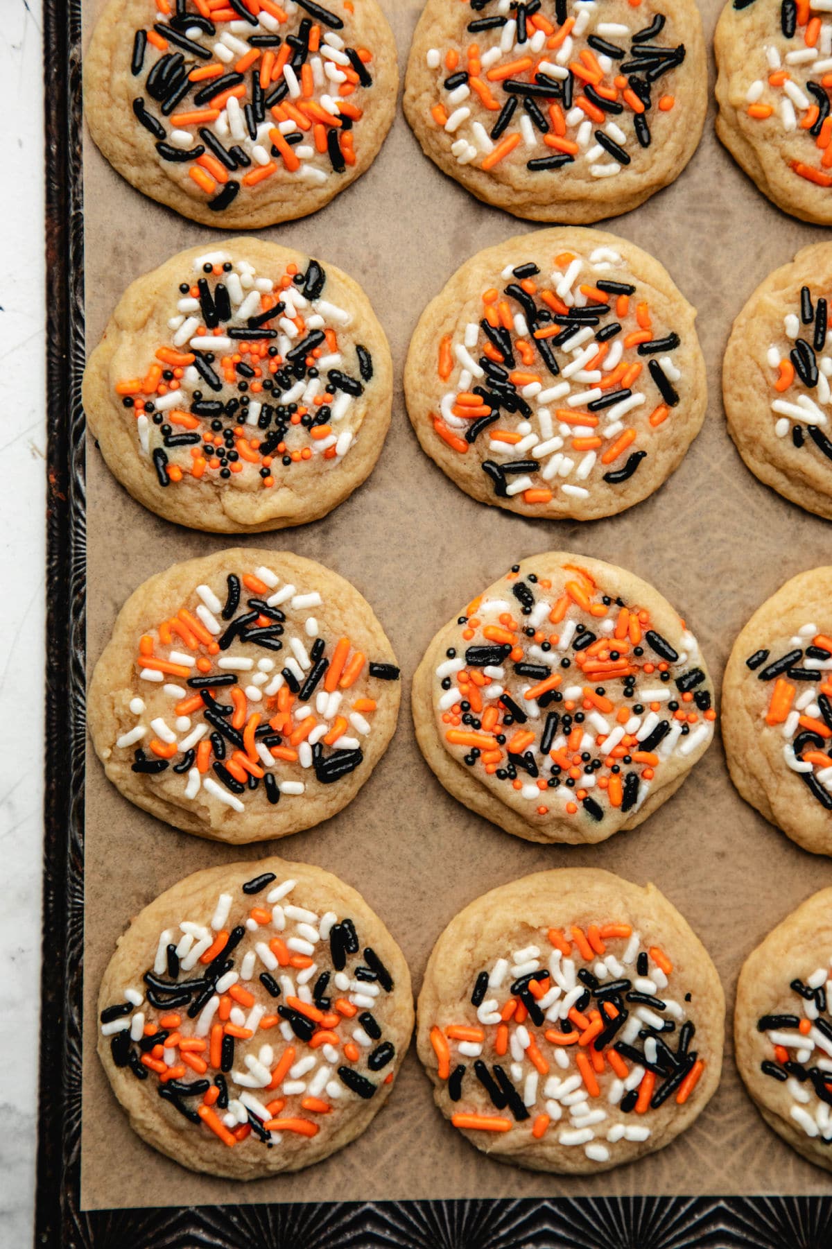 Rows of Halloween sprinkle cookies on a piece of brown parchment paper. 