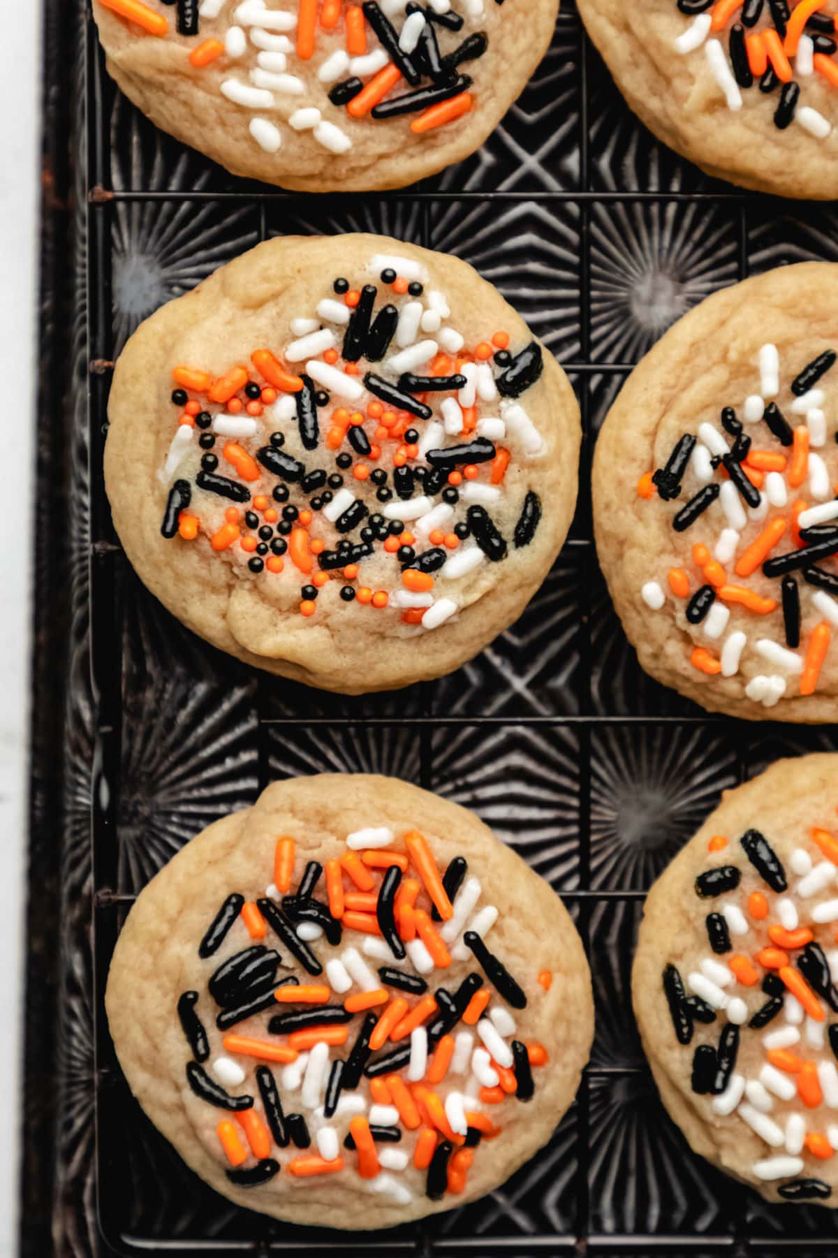 Rows of Halloween sprinkle cookies on a wire cooling rack on a vintage baking sheet. 