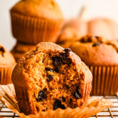 A pumpkin chocolate chip muffin in a muffin liner on a wire cooling rack.