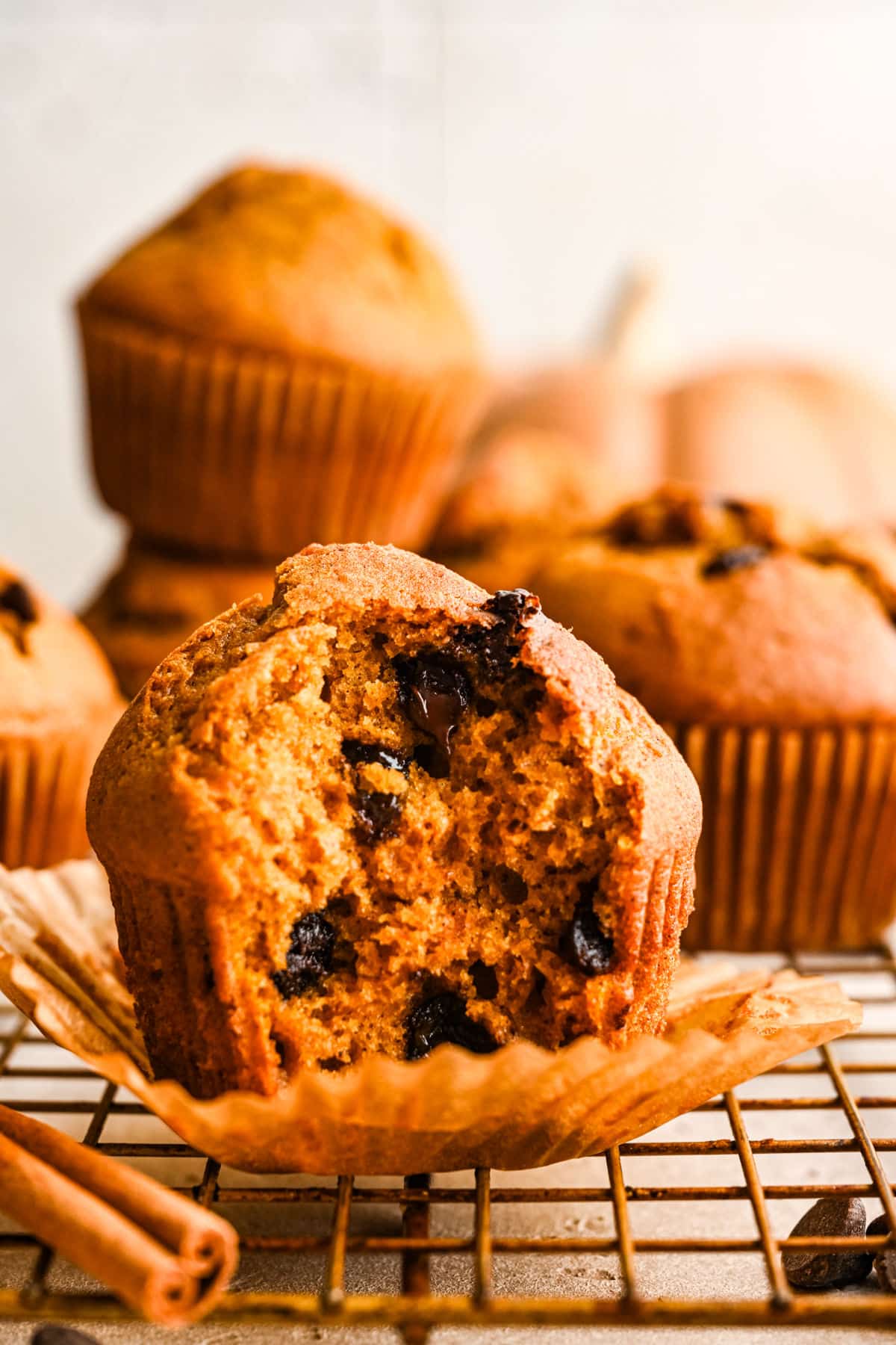 A pumpkin chocolate chip muffin in a muffin liner on a wire cooling rack.