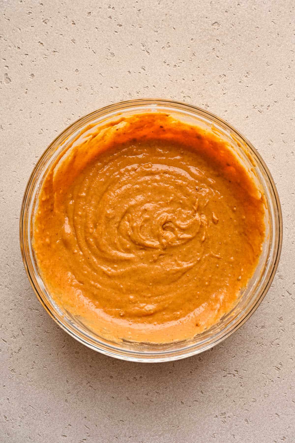 Pumpkin muffin batter in a glass mixing bowl. 