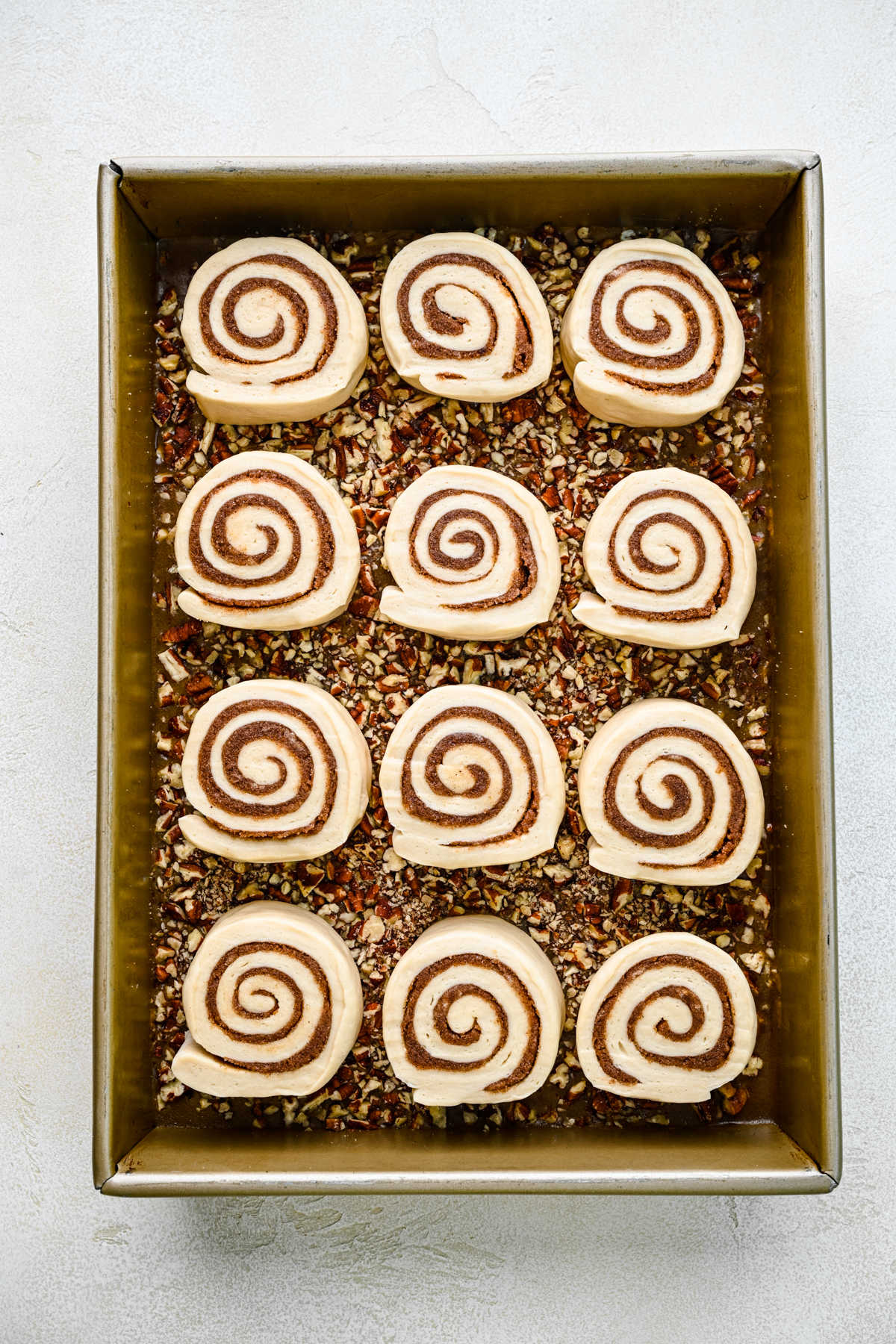 Cut pieces of sticky bun dough on top of sticky bun topping in a metal pan.