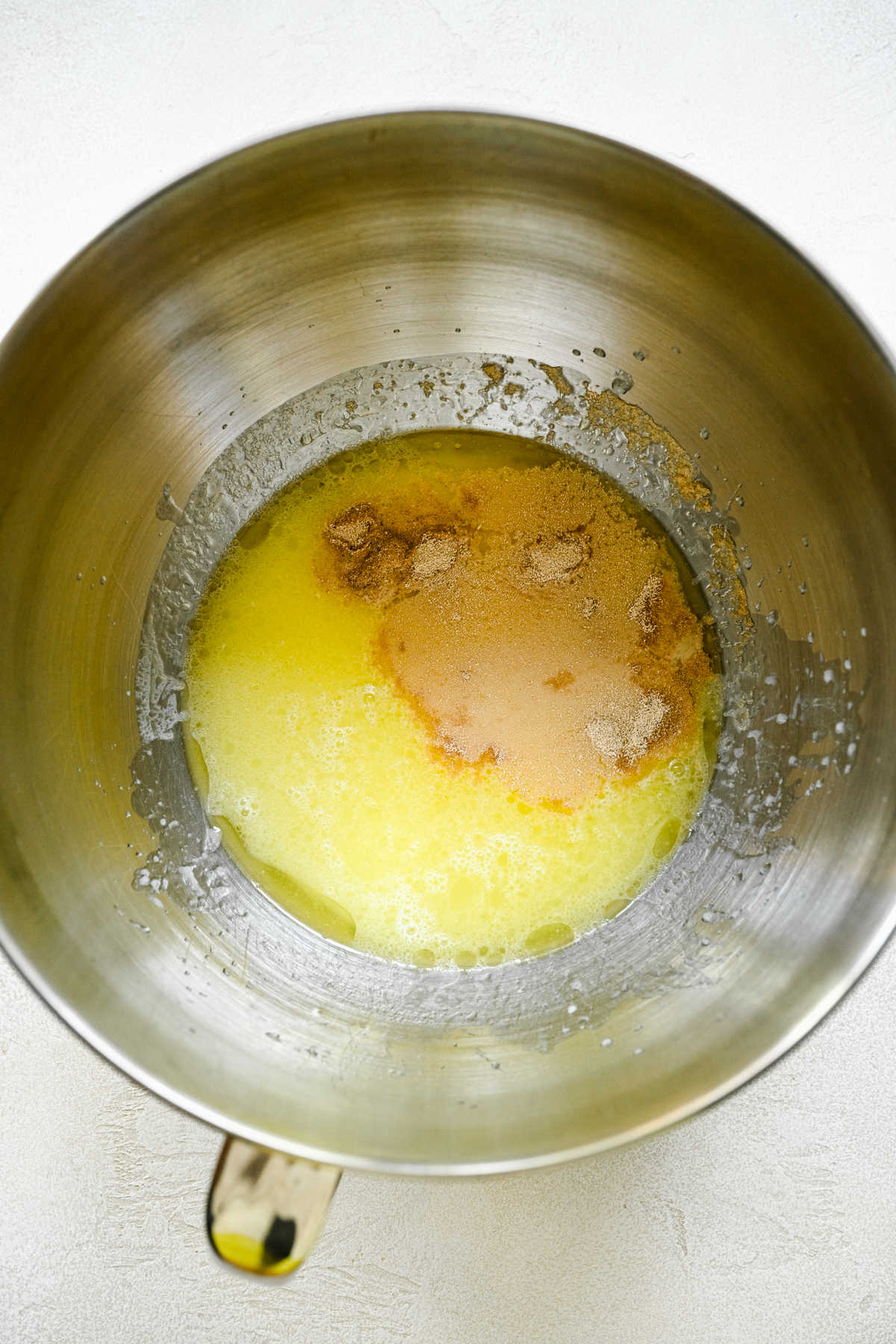 Melted butter mixture and yeast mixture in a silver mixing bowl. 
