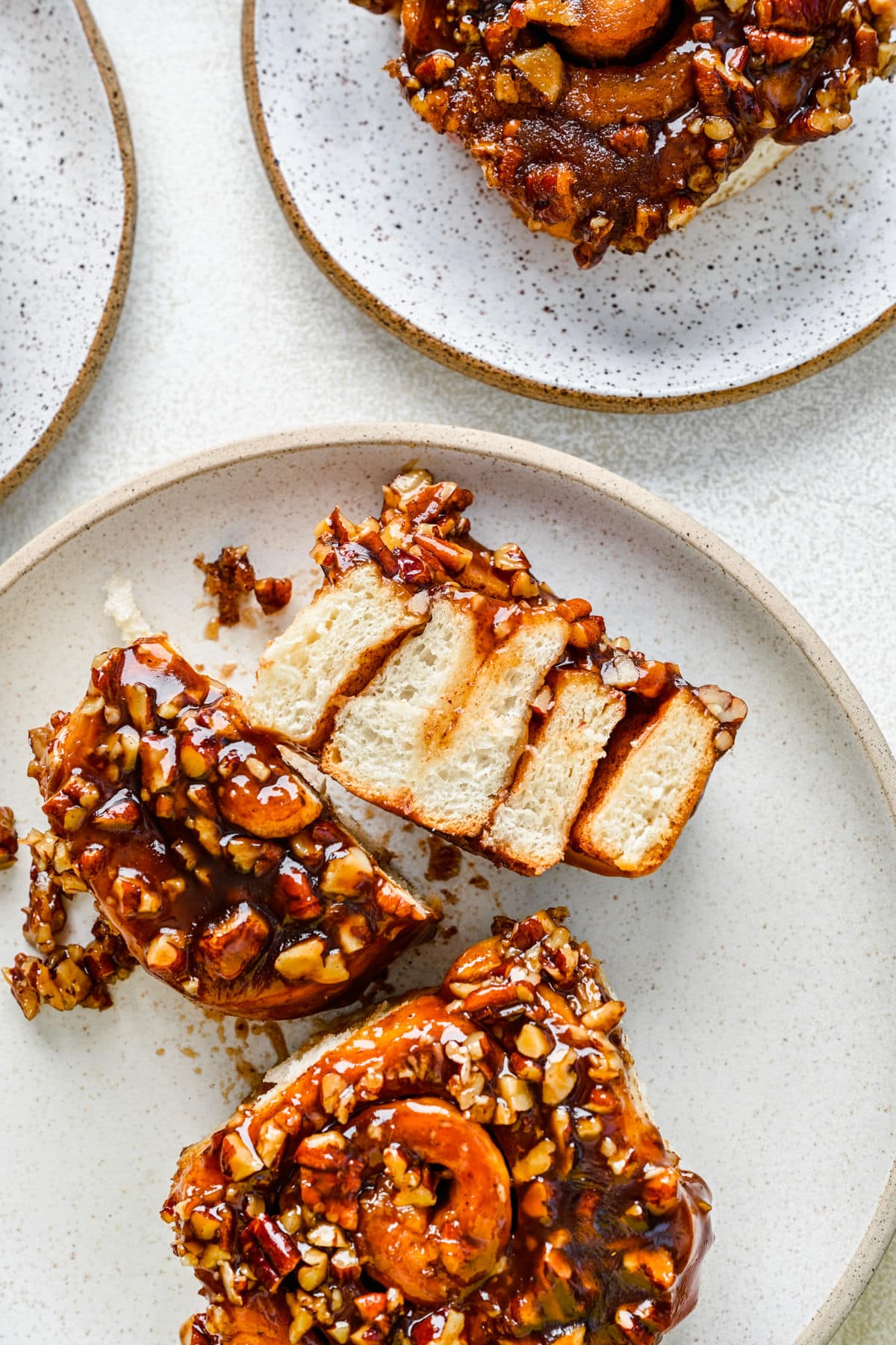 Two sticky buns on a white plate with one sticky bun cut in half. 