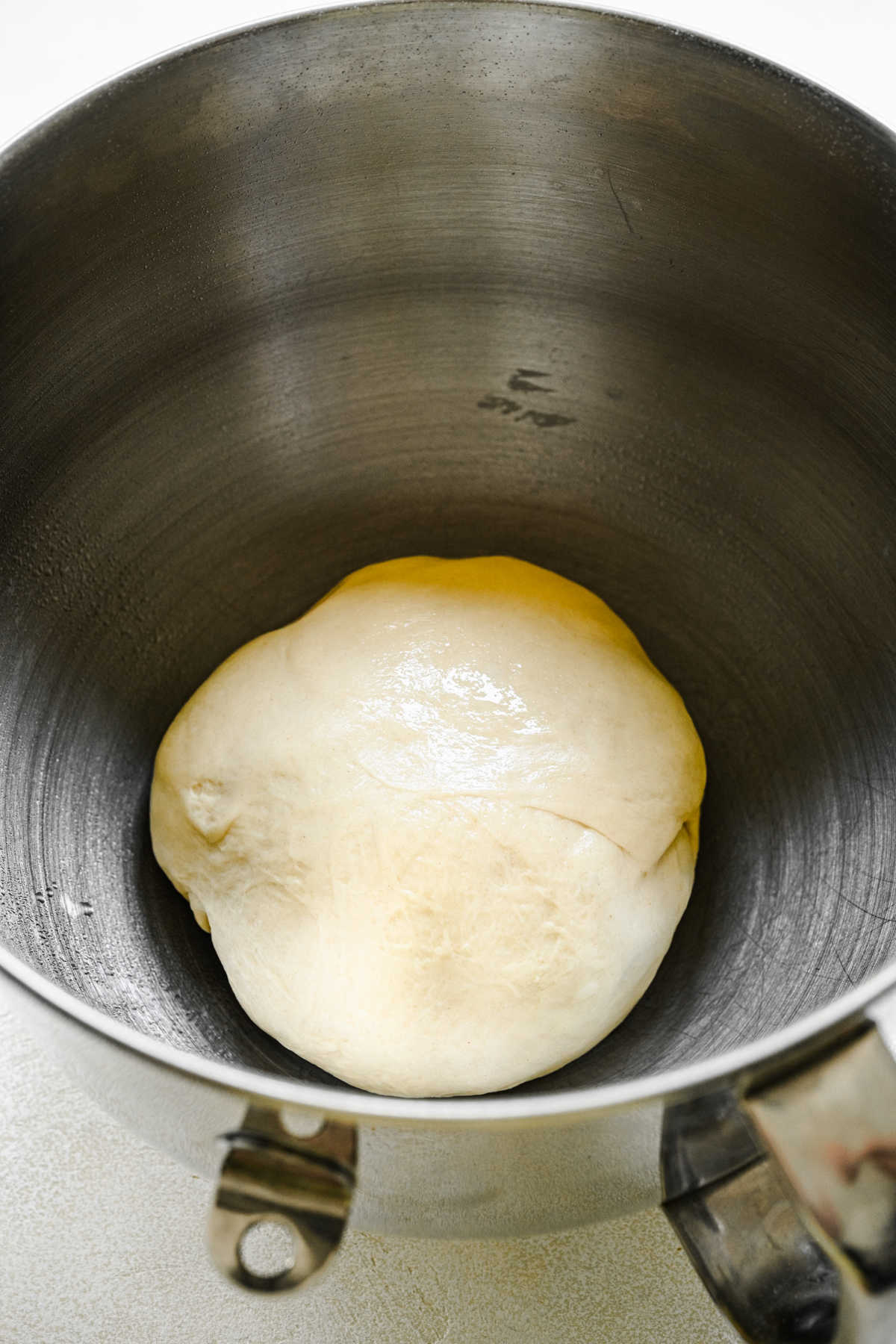 Ball of sticky bun dough in a silver mixing bowl. 