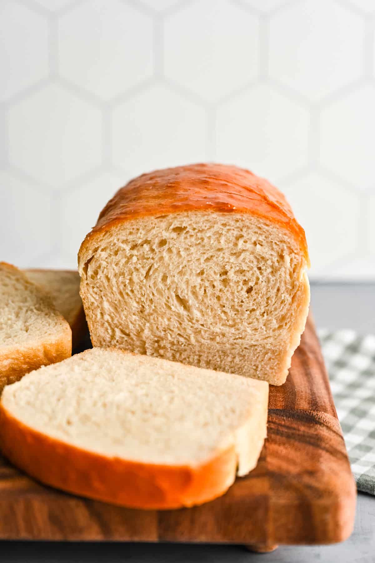 A slice of white bread in front of the loaf of white bread on a wooden cutting board. 