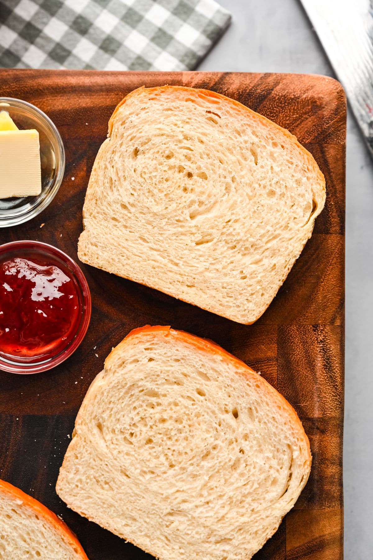 Close up photo of slices of white bread on a wooden cutting board next to a checkered kitchen linen.