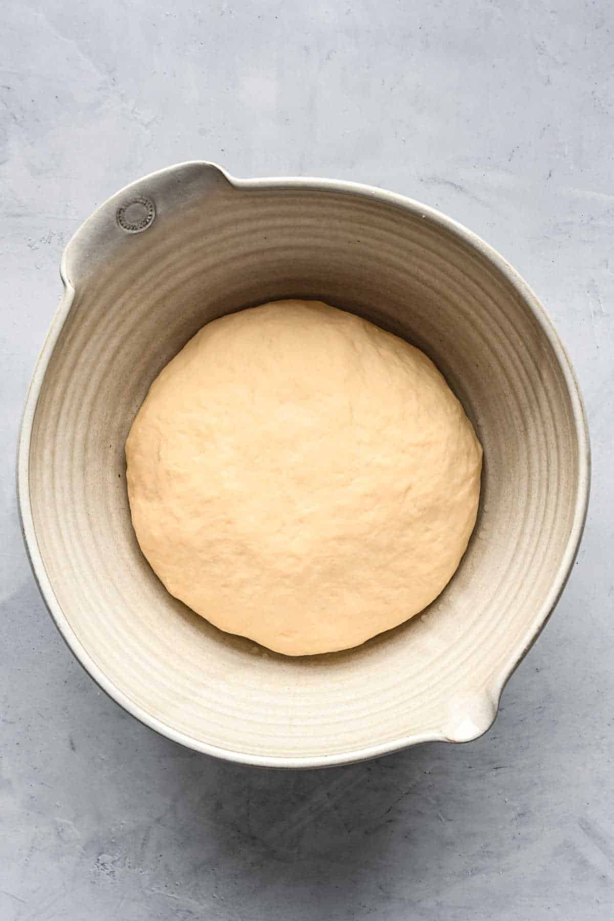 A ball of white bread dough in a ceramic mixing bowl. 