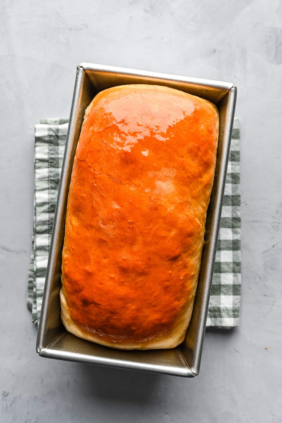A baked loaf of homemade white bread brushed with melted butter.