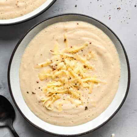 Two bowls of Wisconsin cauliflower soup topped with shredded cheddar cheese.