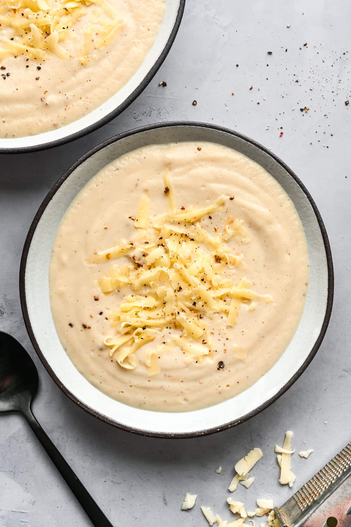 Two bowls of Wisconsin cauliflower soup topped with shredded cheddar cheese.