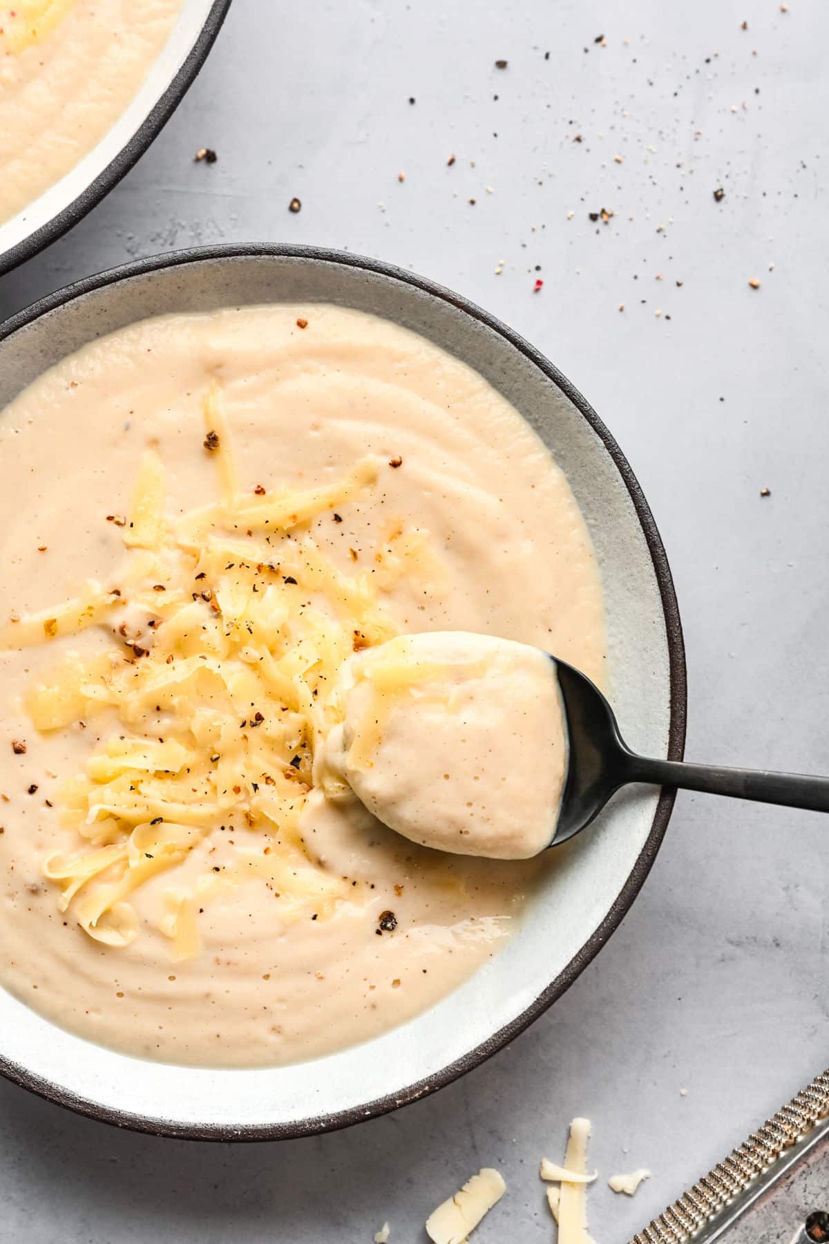 A black spoon holding a spoonful of Wisconsin cauliflower soup in a bowl of the soup.