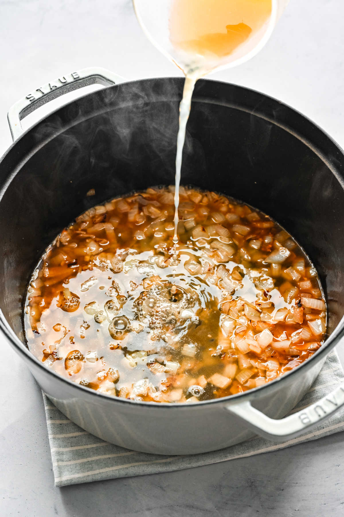 Chicken broth pouring into sauteed onion and garlic. 