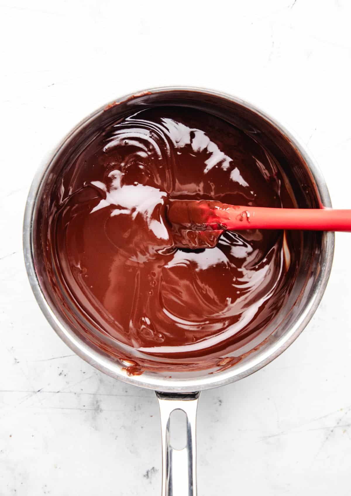Melted butter and chocolate in a saucepan with a red spatula in it. 