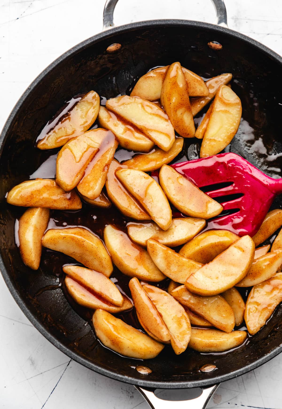 A pink spatula stirring vanilla extract into cinnamon apples. 