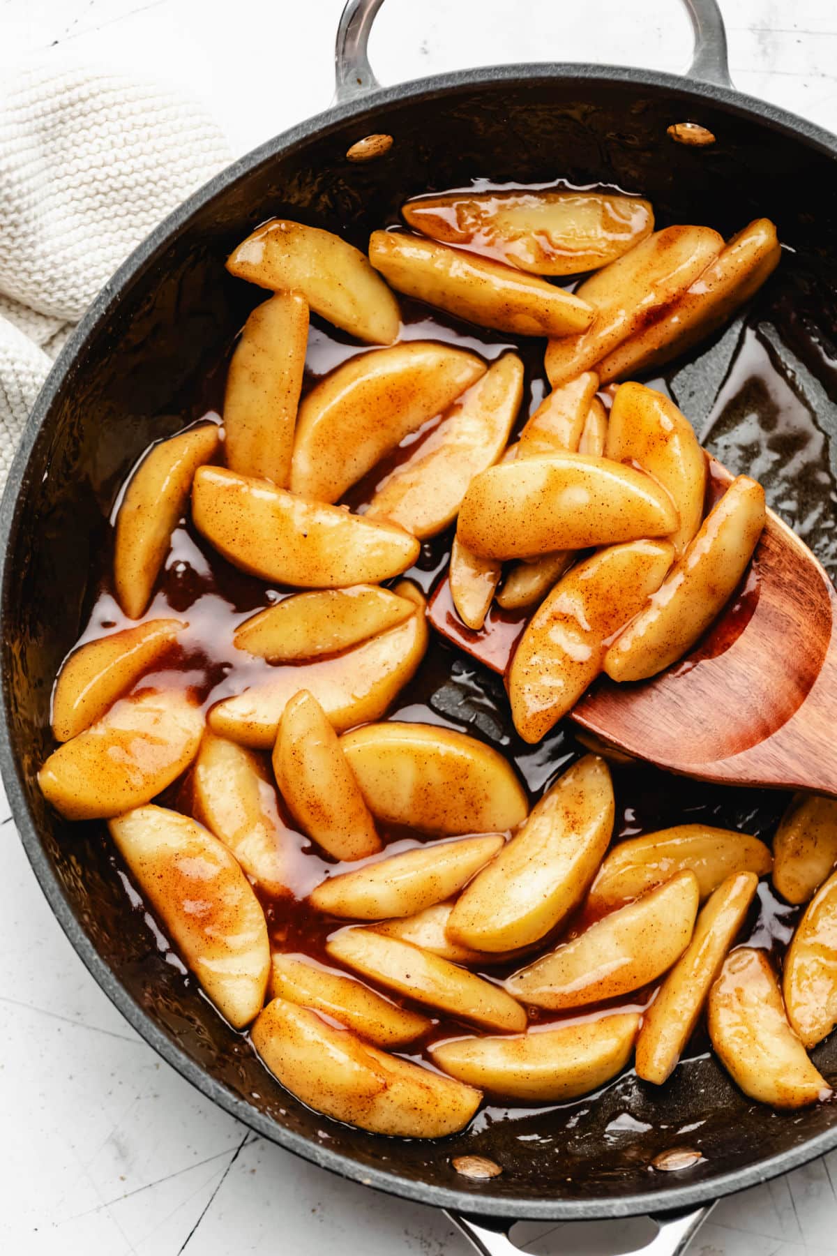 A cast iron skillet filled with sauteed cinnamon apples next to a tan kitchen linen.
