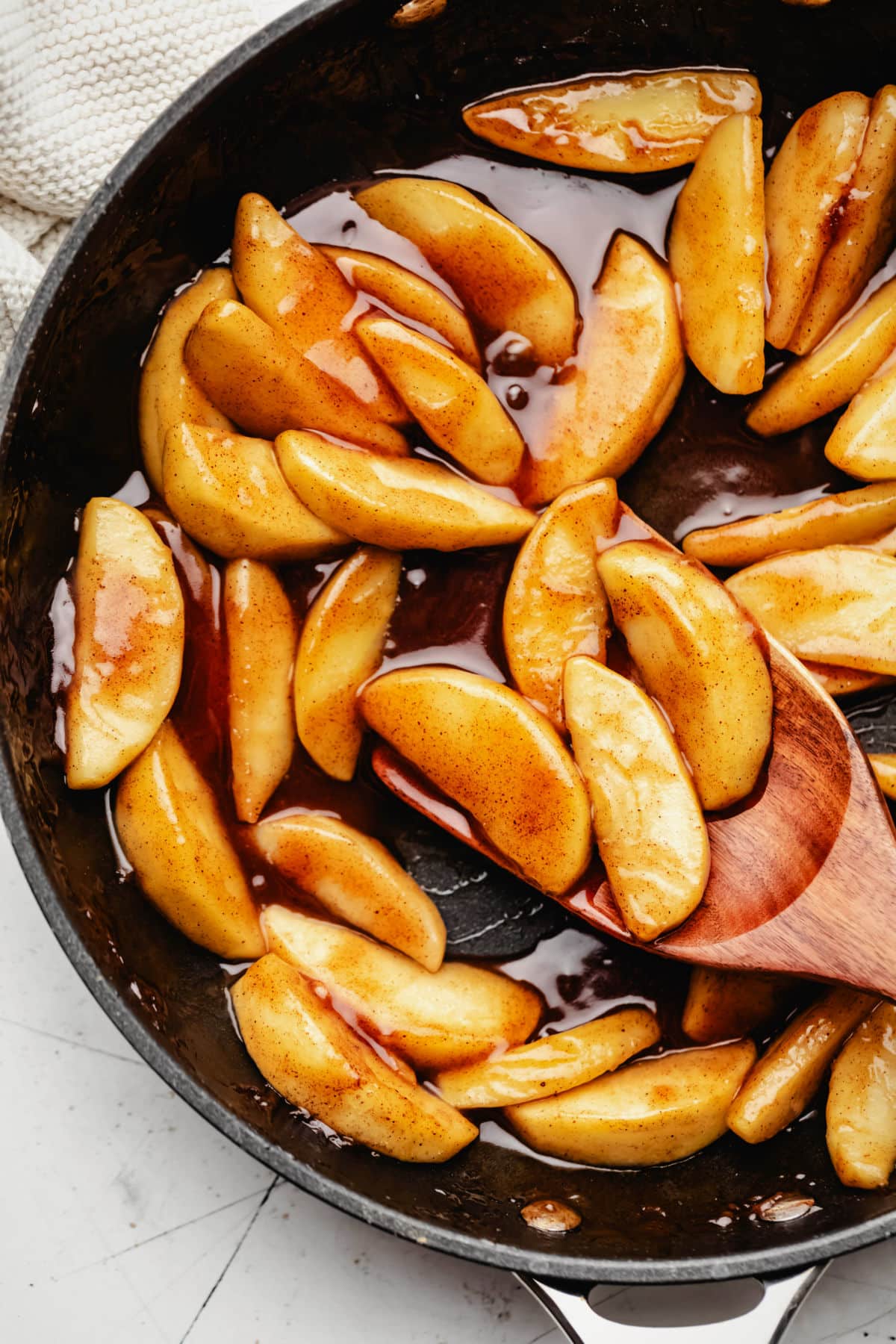 A wooden spoon scooping up cinnamon apples in a cast iron skillet.