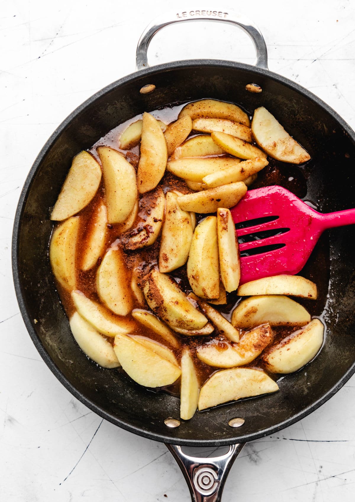 A pink spatula stirring brown sugar and cinnamon into apple slices. 