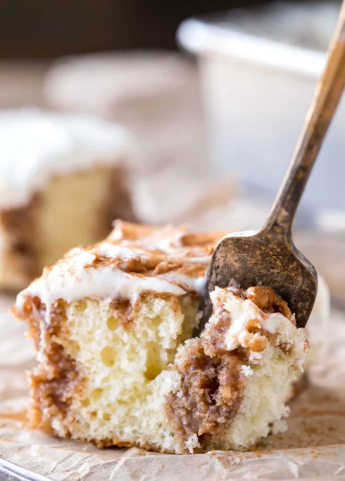A vintage fork taking a bite of a piece of cinnamon roll poke cake.