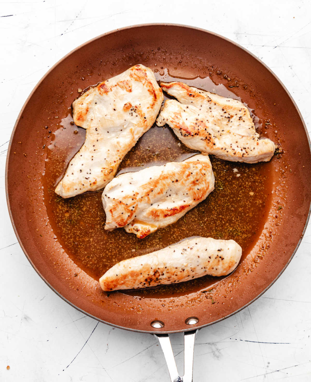 Four seasoned chicken breast halves in maple mustard sauce in a skillet.