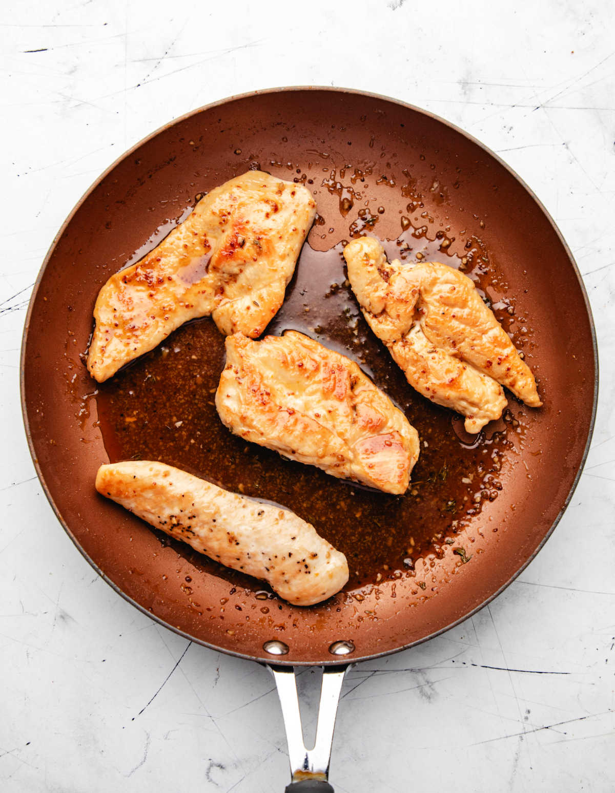 Baked maple mustard chicken in sauce in a skillet.