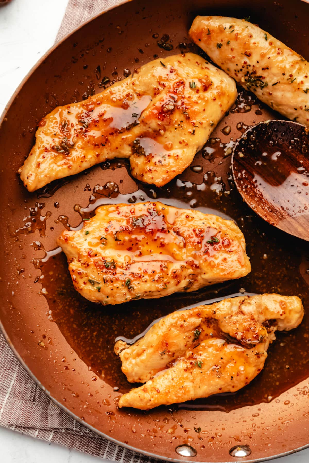 Maple mustard chicken in a copper skillet with a wooden spoon holding the maple mustard sauce.