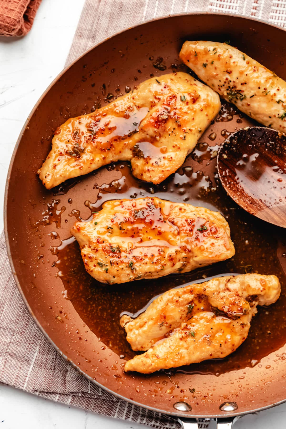 A copper skillet with four maple mustard chicken breasts in it. 