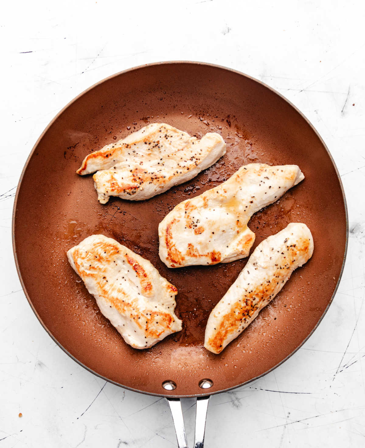 Four seasoned chicken breast halves in a copper skillet.