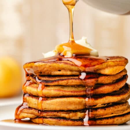 Maple syrup pouring onto a stack of pumpkin pancakes.