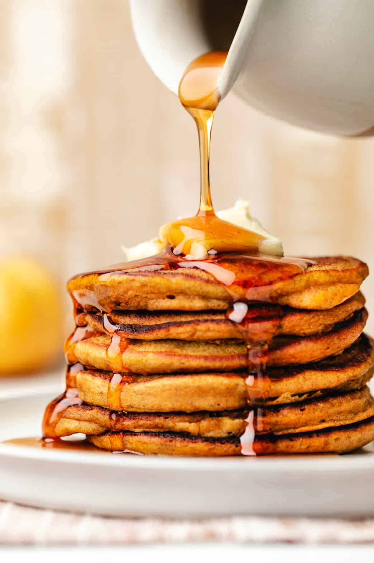 Maple syrup pouring onto a stack of pumpkin pancakes.