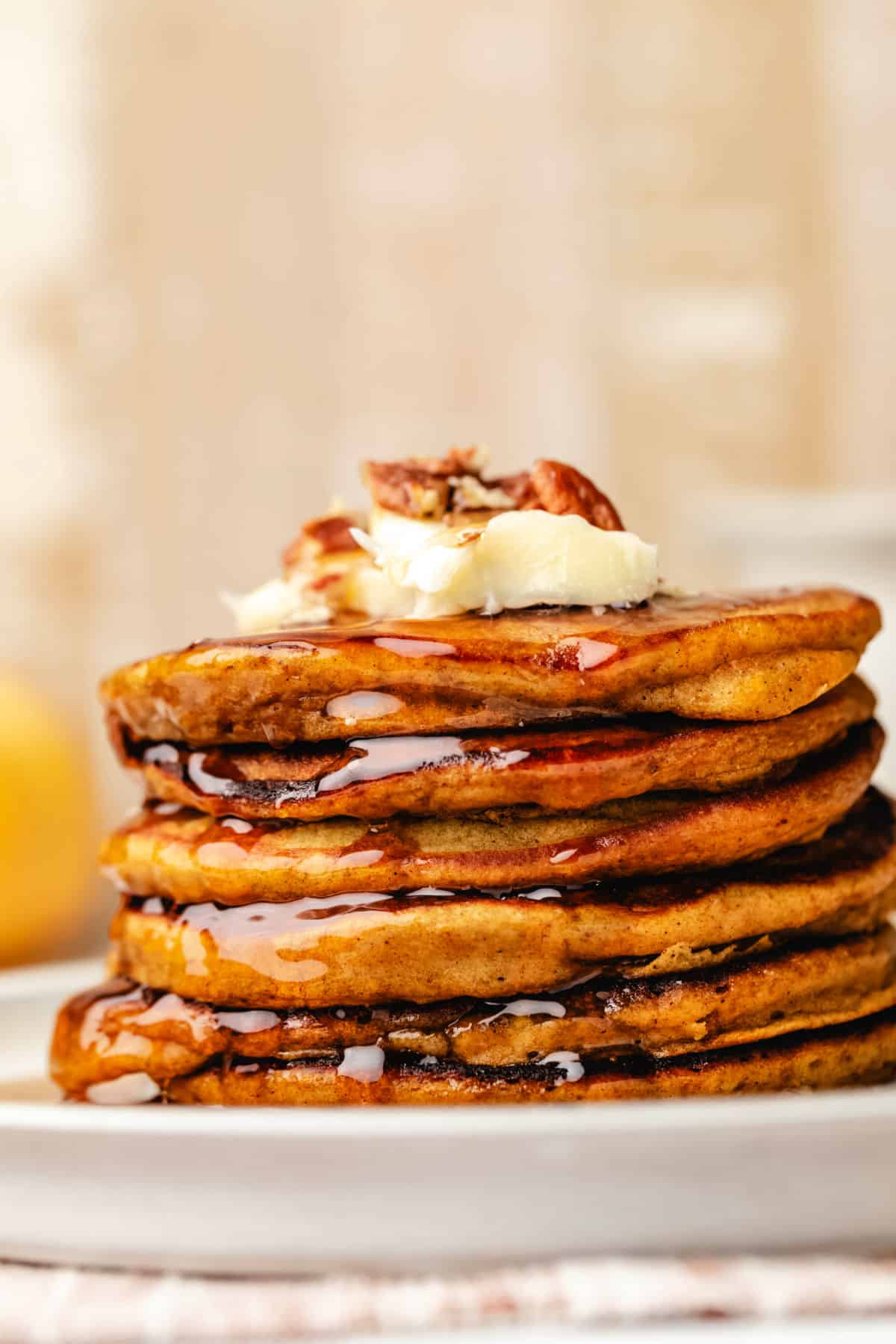 A stack of pumpkin pancakes topped with butter and chopped pecans.