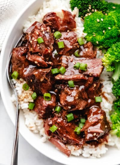 Close up photo of slow cooker Korean beef over white rice next to steamed broccoli.