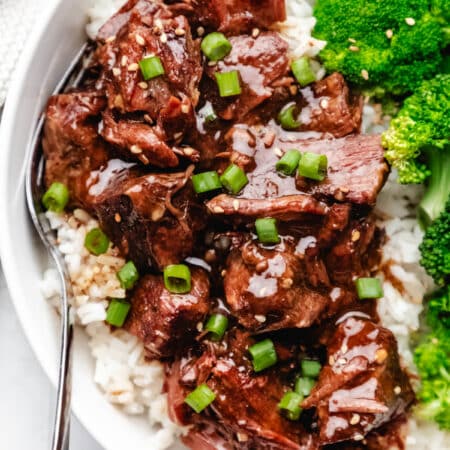 Close up photo of slow cooker Korean beef over white rice next to steamed broccoli.