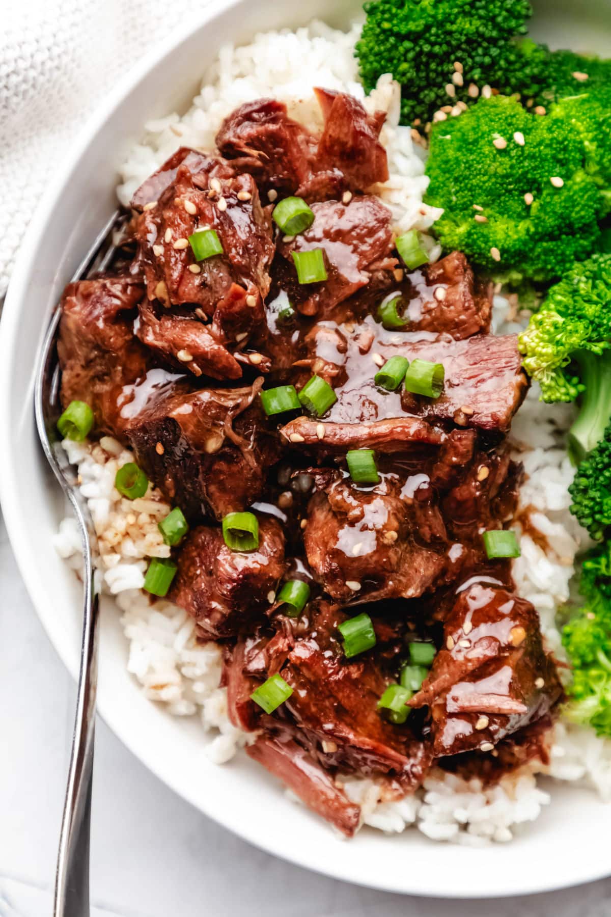 Close up photo of slow cooker Korean beef over white rice next to steamed broccoli.