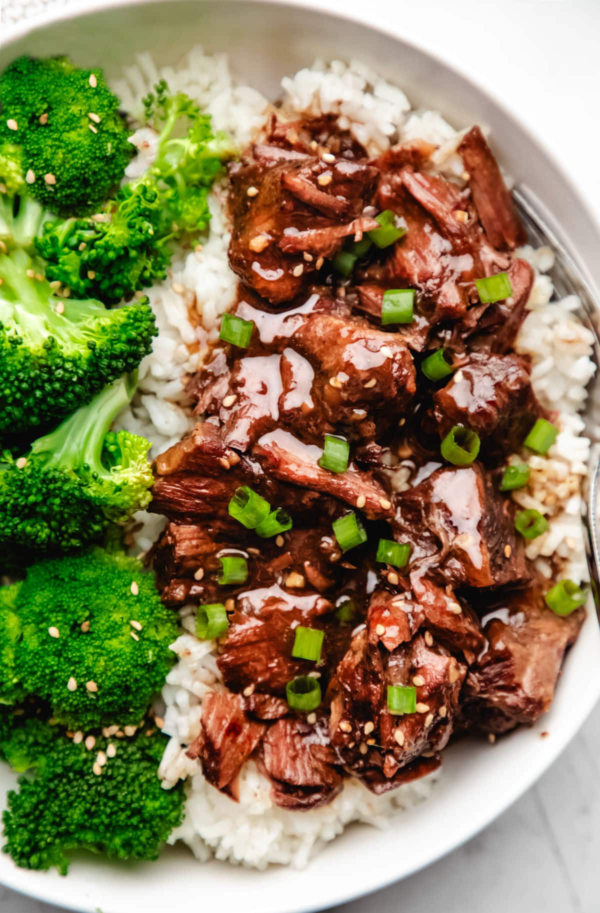 Slow cooker Korean beef in a white bowl topped with green onions and sesame seeds. 