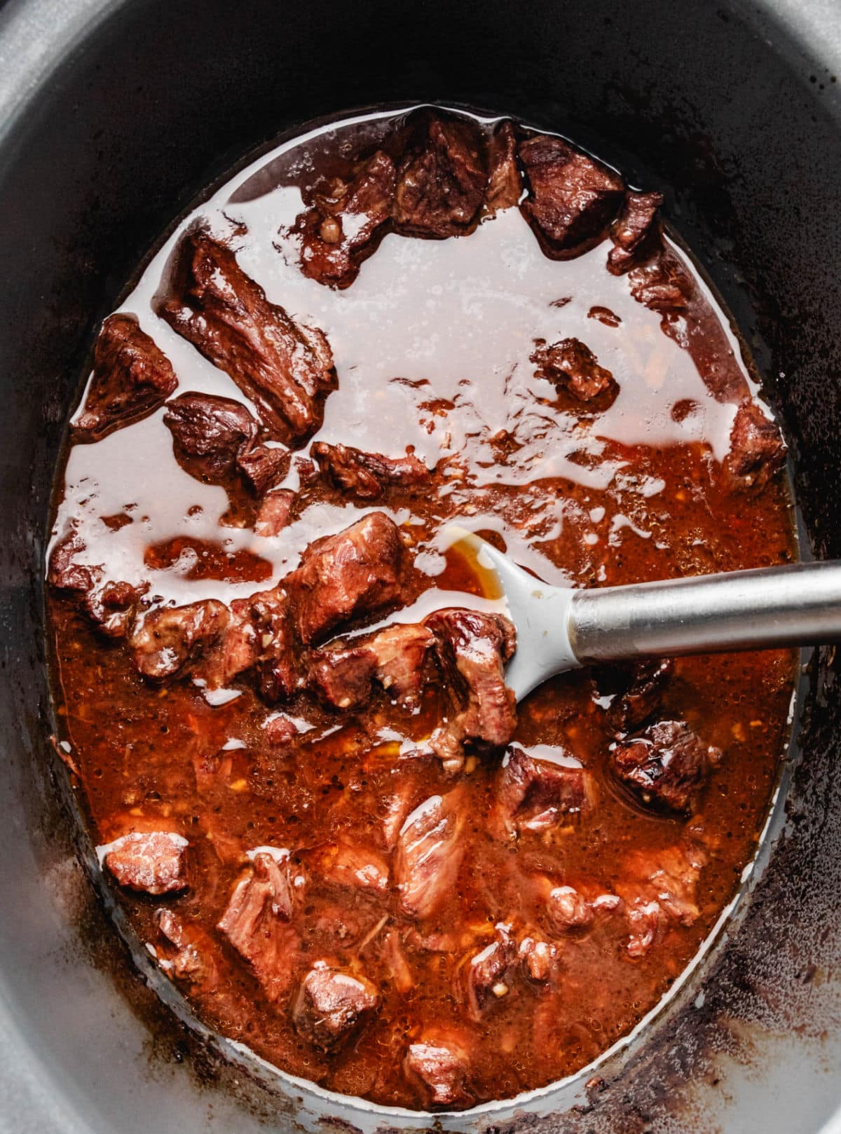 A silver spoon lifting up pieces of Korean beef from a slow cooker. 