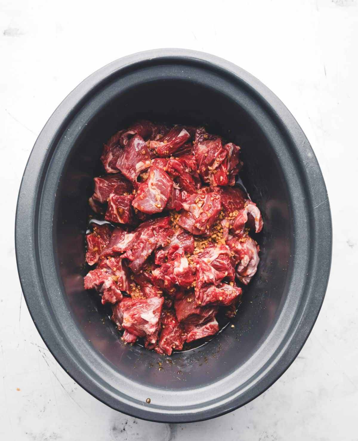 Korean sauce poured over chuck roast cubes in a slow cooker insert. 